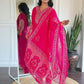 Woman wearing a bright pink embroidered traditional outfit in a room with a mirror and plant.