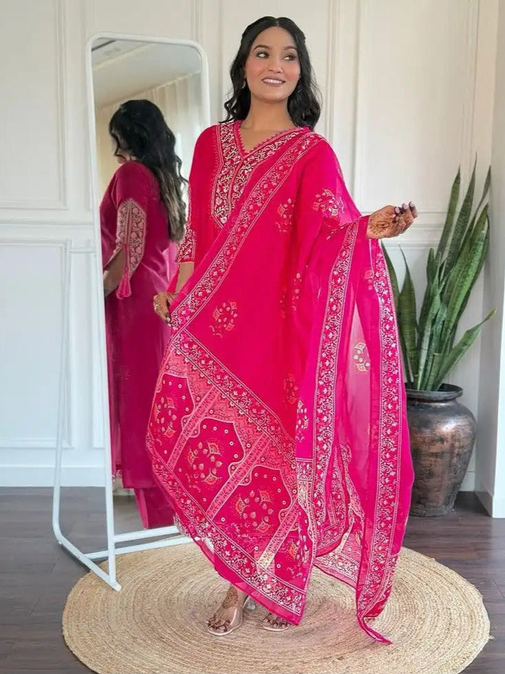 Woman wearing a bright pink embroidered traditional outfit in a room with a mirror and plant.