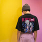 Person wearing a black t-shirt with graphic design and text, standing against a yellow and pink background.
