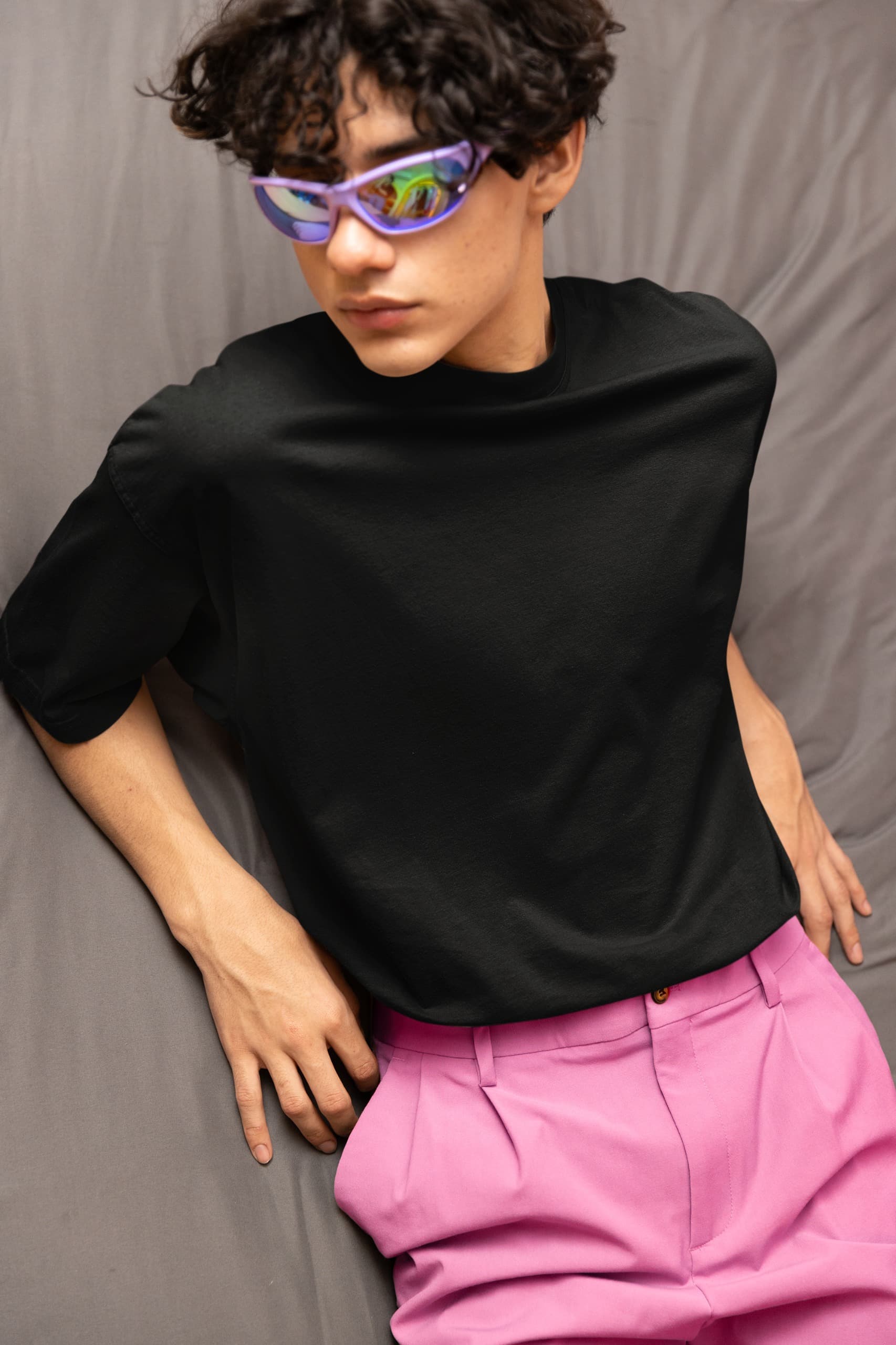 Person wearing a black turtleneck and pink pants with colorful sunglasses against a gray background