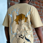 Person wearing a beige t-shirt with graphic design in front of a brick wall